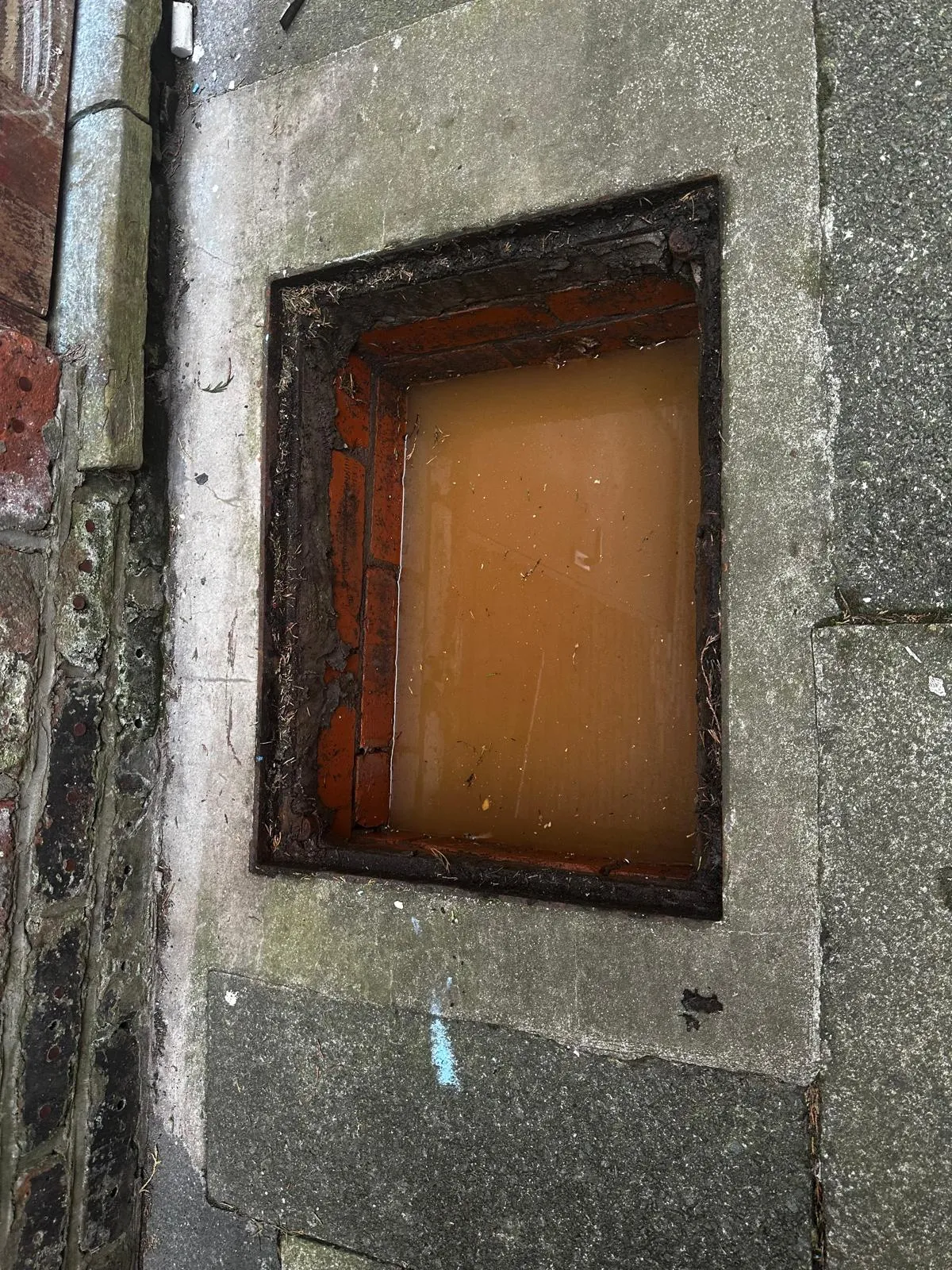An overflowing external drain full of dirty water, highlighting a severe blockage.