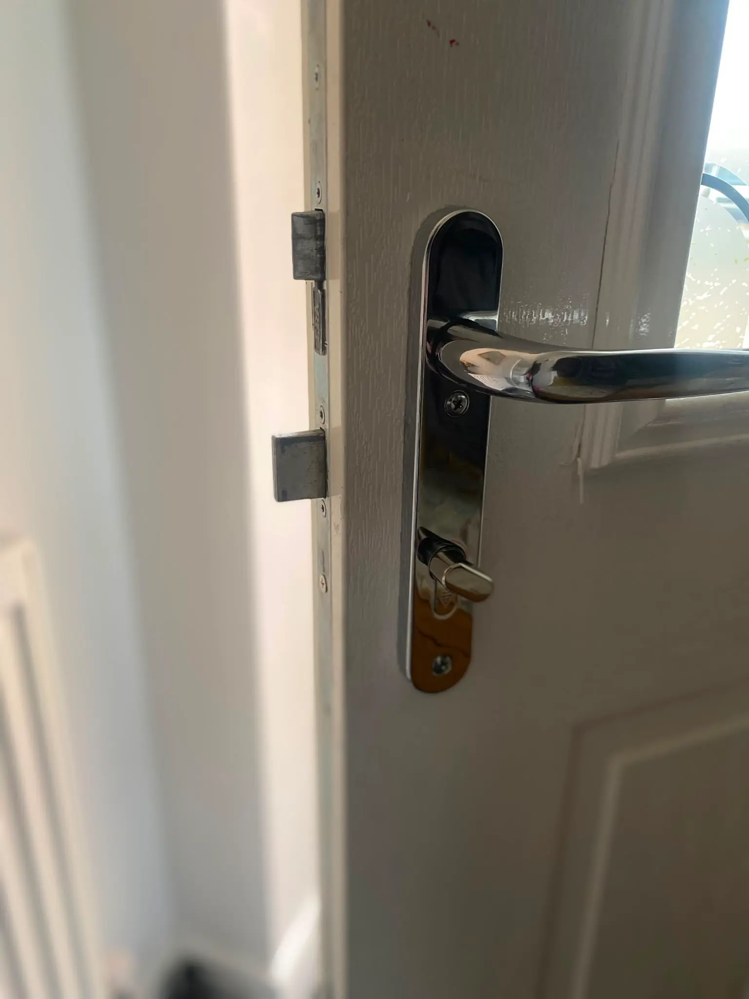 Close-up of a chrome door handle, thumbturn lock, and multi-point locking mechanism on a white uPVC door