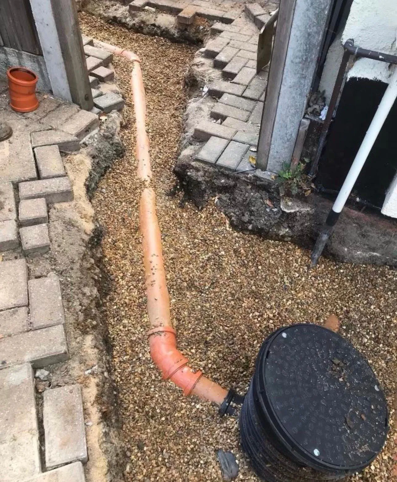 New orange underground drain pipe installation in a gravel trench with a manhole chamber during groundworks.