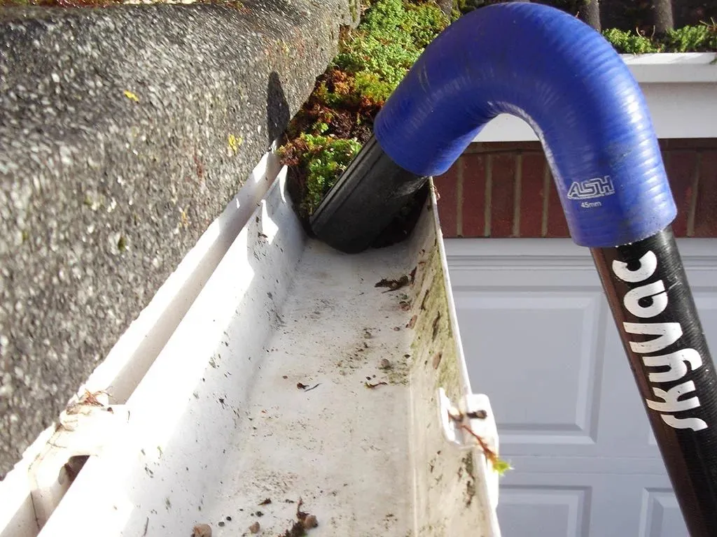 A high-reach vacuum system being used to clear moss from a residential guttering system.