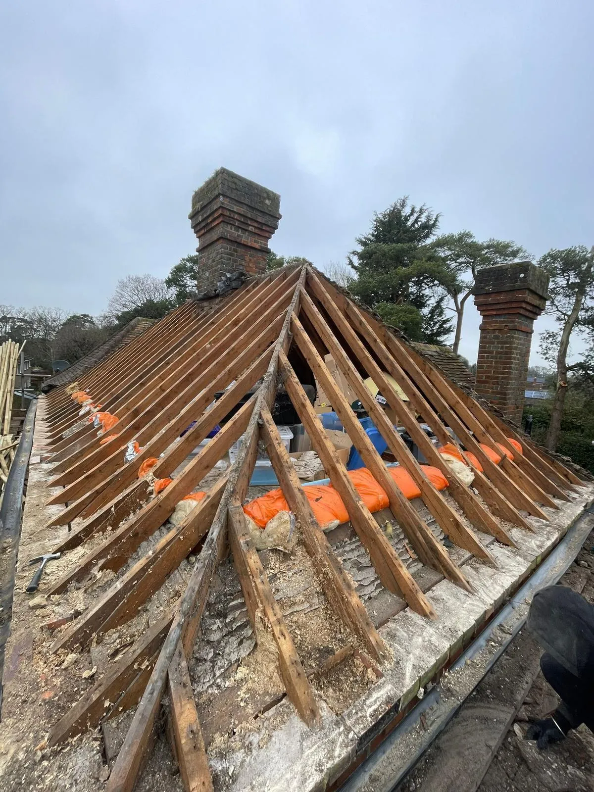 Roof stripped down to timber battens and rafters during a full re-roofing project, preparing for new tiles or slates, with two chimney stacks in view.