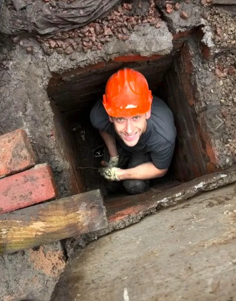 A KO Drainage engineer in an orange hard hat looking up from an excavated trench during a drain repair.