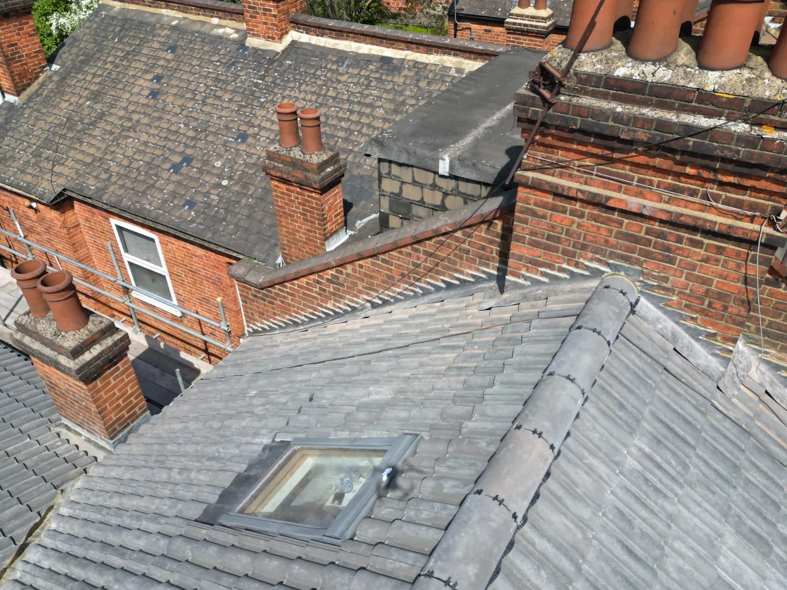 Aerial view of residential rooftops with tiled pitched roofs, a skylight, chimneys, and a flat roof section, indicating comprehensive roofing services.