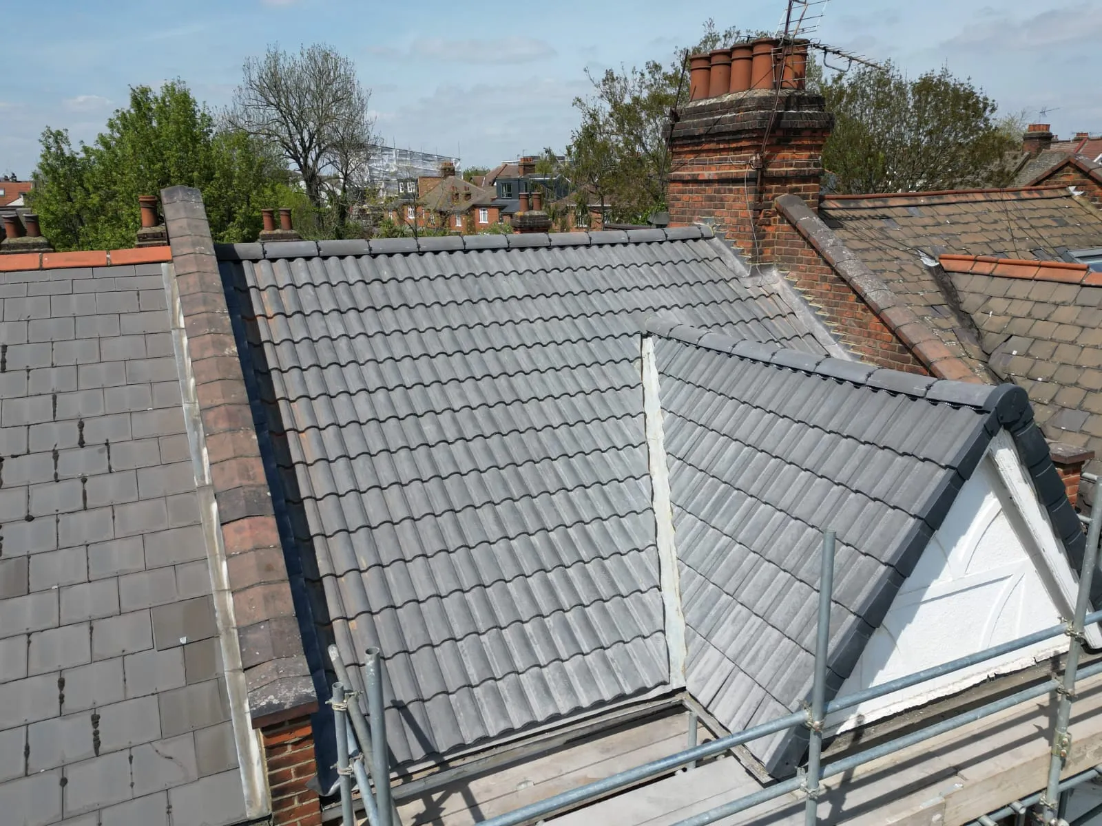 Newly installed grey tiled pitched roof with a dormer window during a re-roofing project, showing scaffolding and a brick chimney.