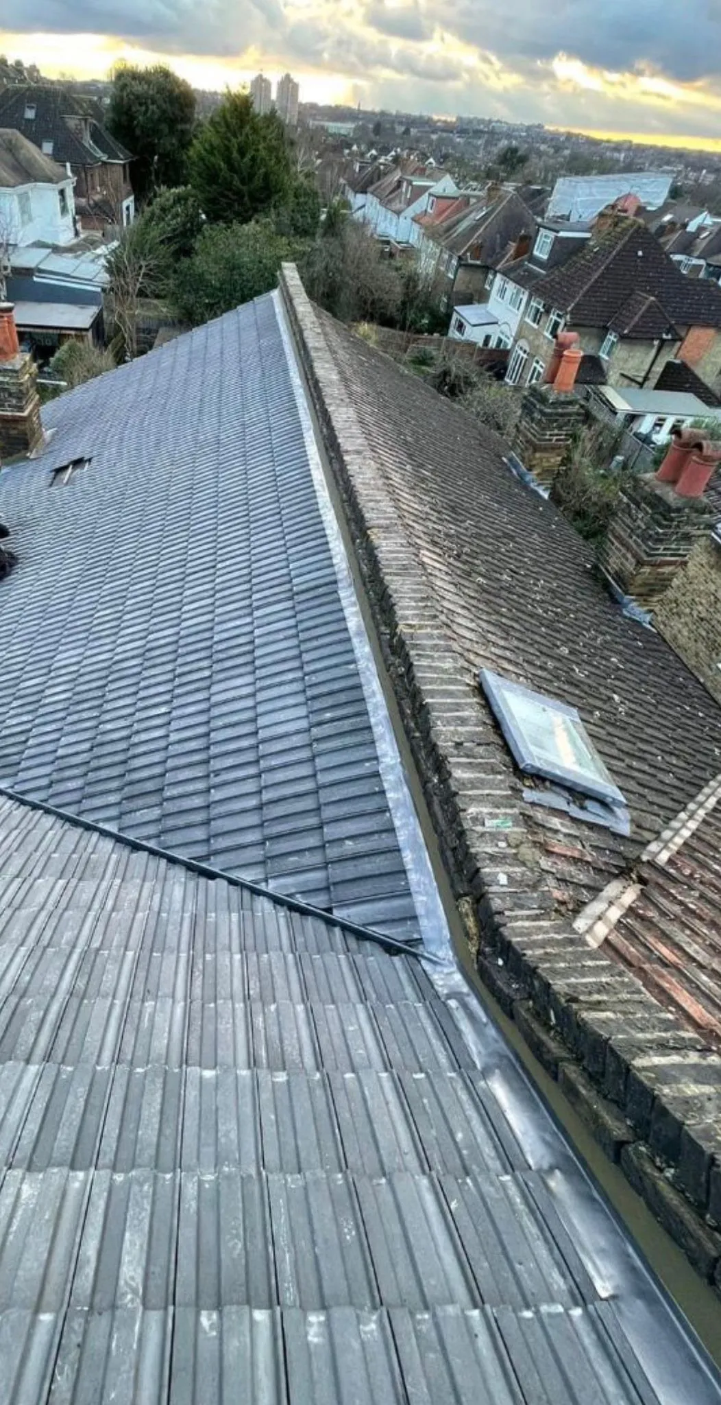Newly installed grey roof tiles next to an old tiled roof section with a lead valley