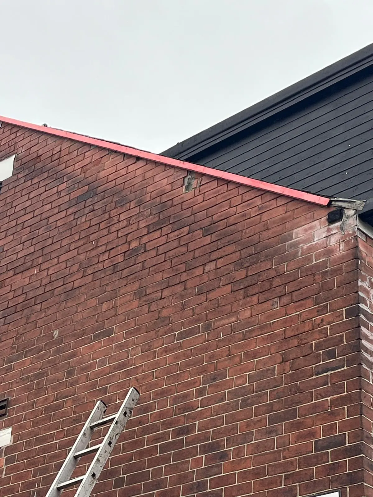 A ladder leaning against a brick gable wall of a residential property for roofline inspection