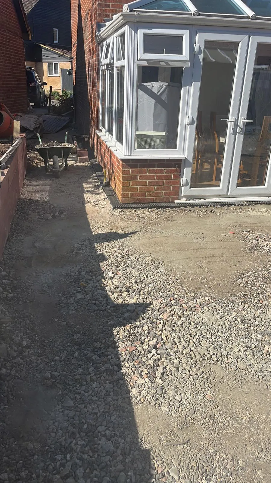 Groundwork in progress for a new driveway or patio, with a gravel sub-base and linear drainage system installed next to a conservatory.