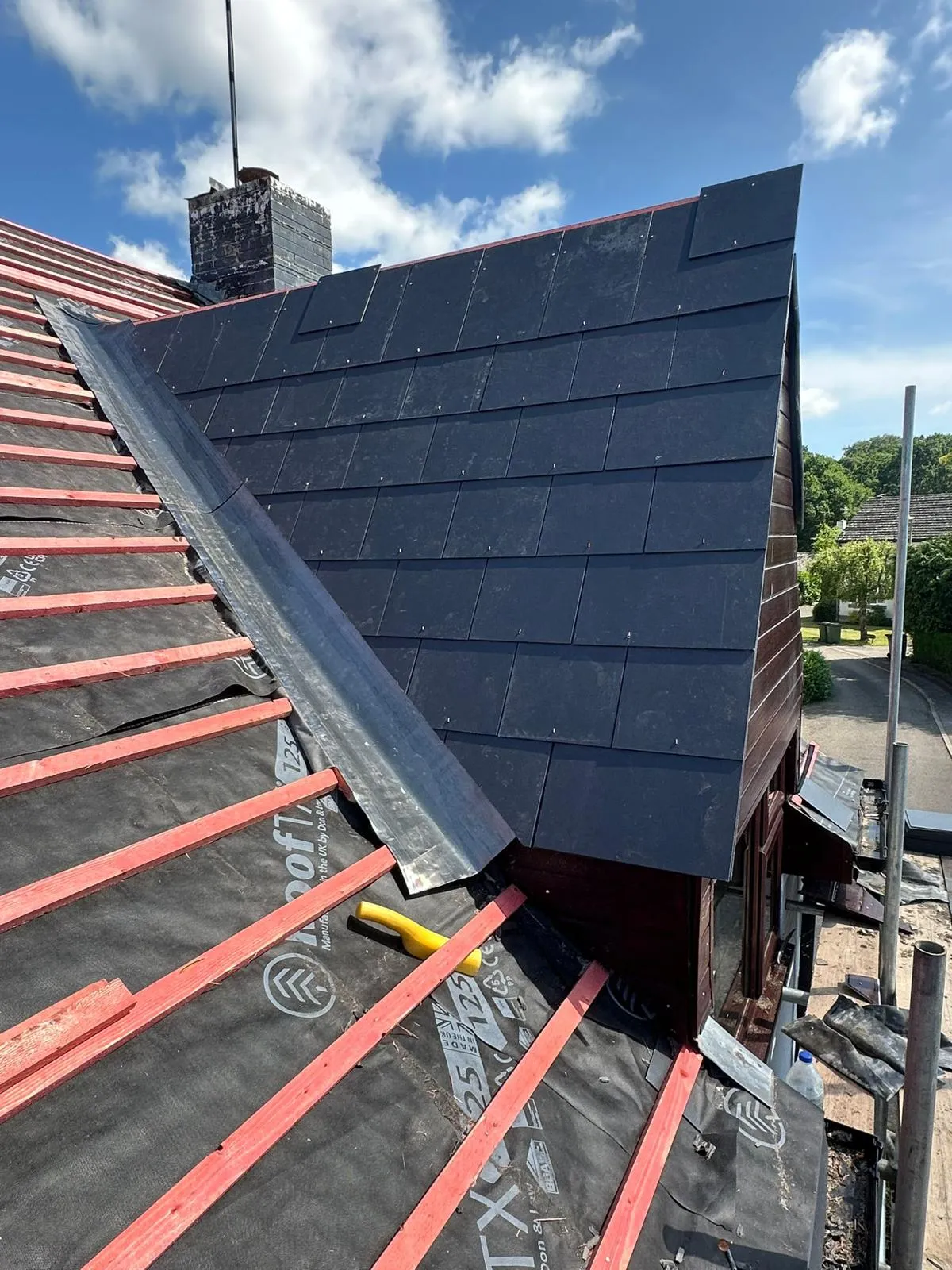 A section of a new roof installation with dark tiles, a lead valley, and the roof underlayment and timber battens visible on the adjoining section.