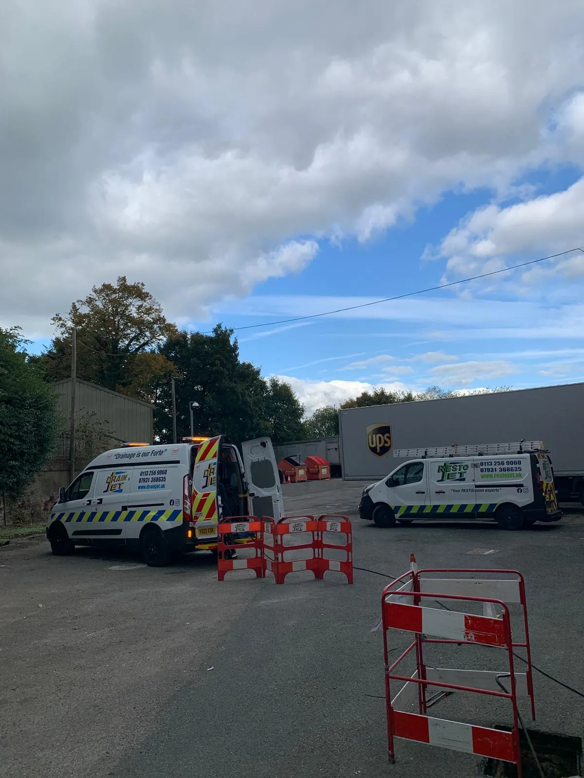 Drain Jet commercial service vans on-site at a business premises in Leeds with safety barriers in place.