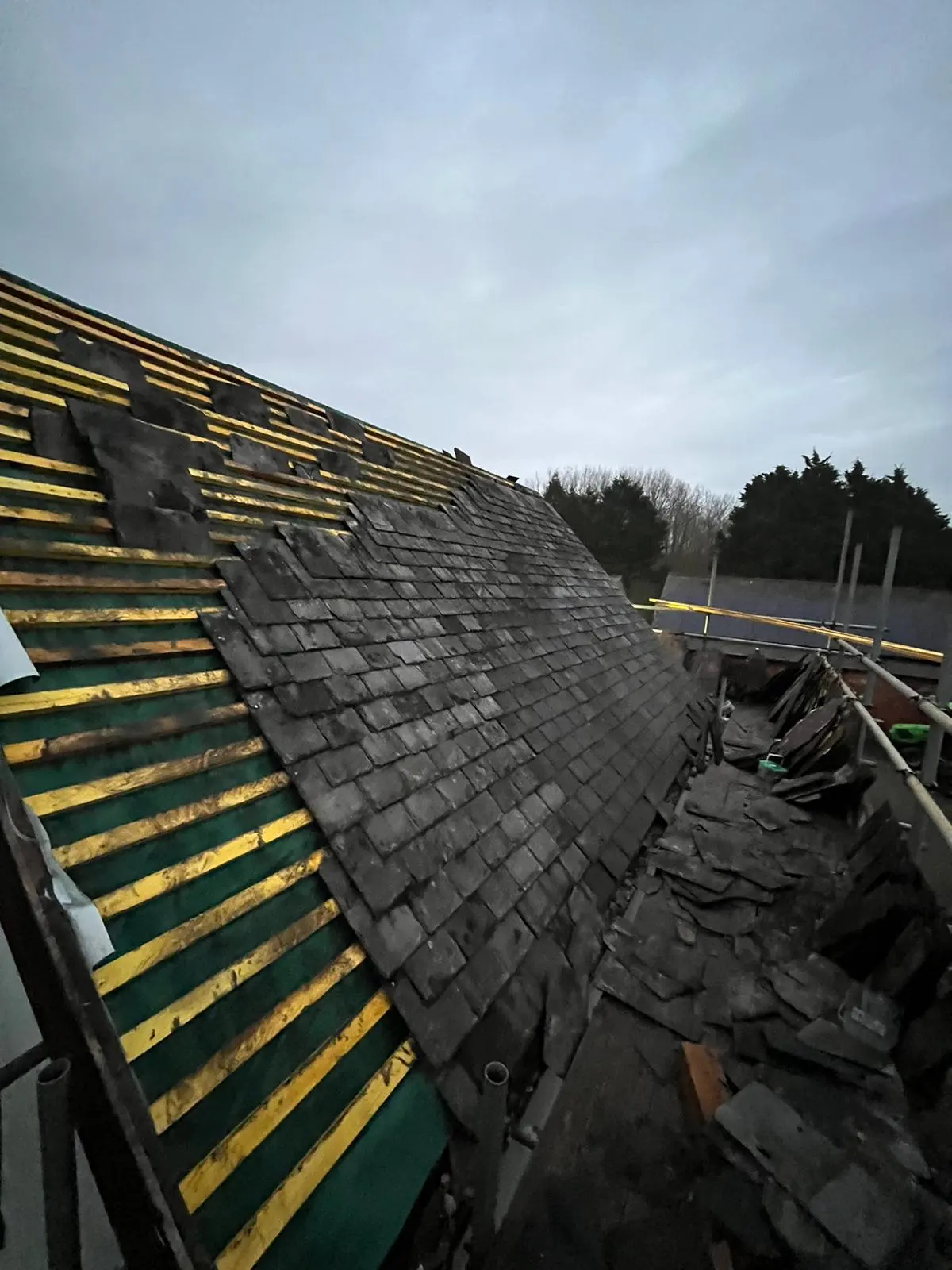 Slate roof replacement in progress showing exposed battens, breathable membrane, and new slates being installed.