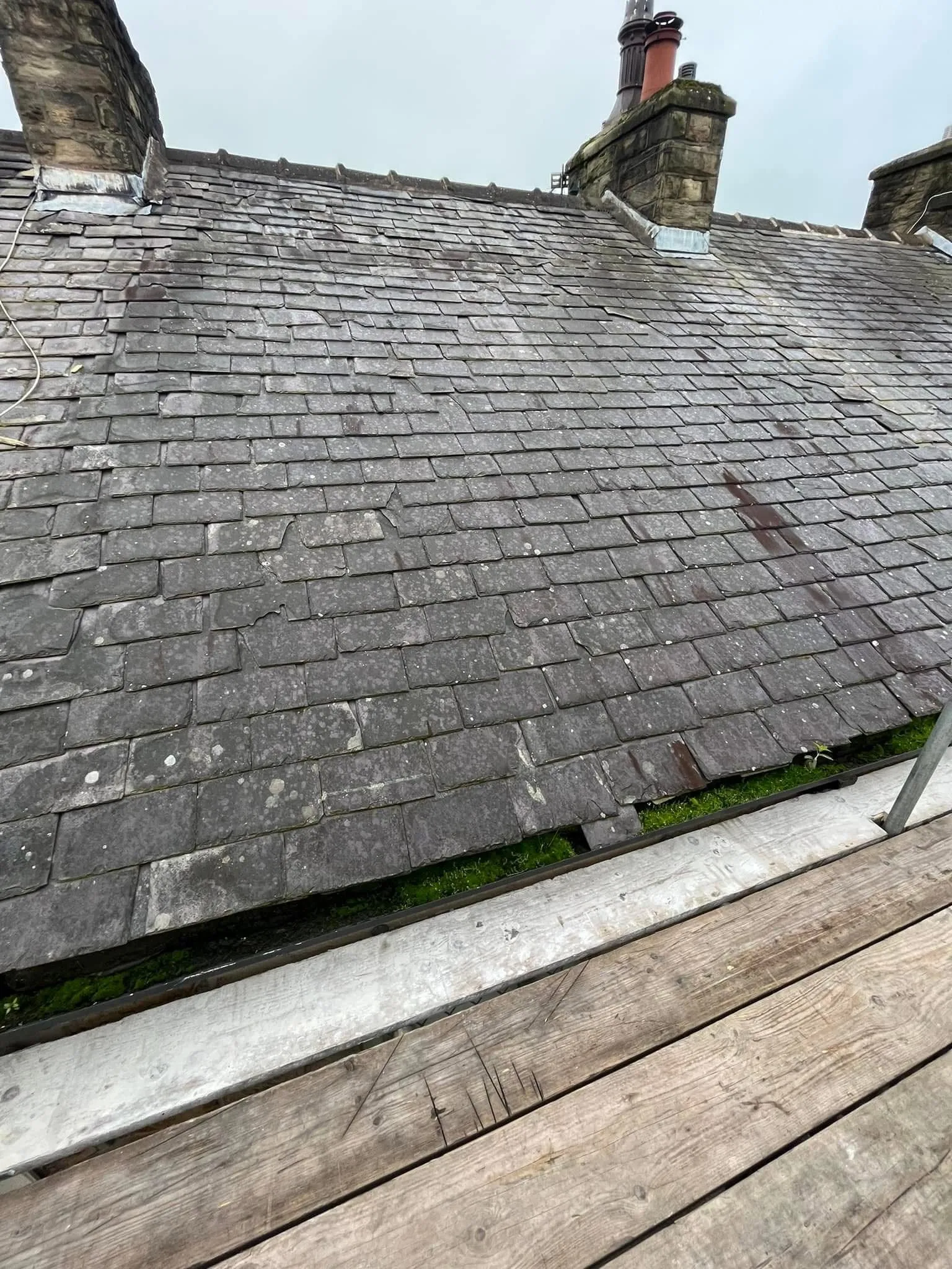 A weathered slate roof with slipped tiles and moss growth, showing the need for repair or replacement by a professional roofer.