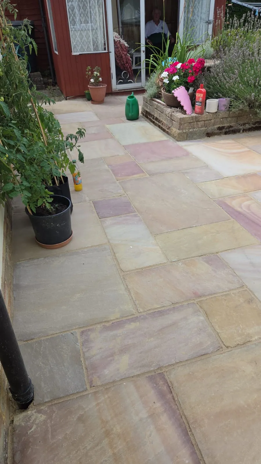 A multi-coloured natural Indian Sandstone patio in a well-maintained garden