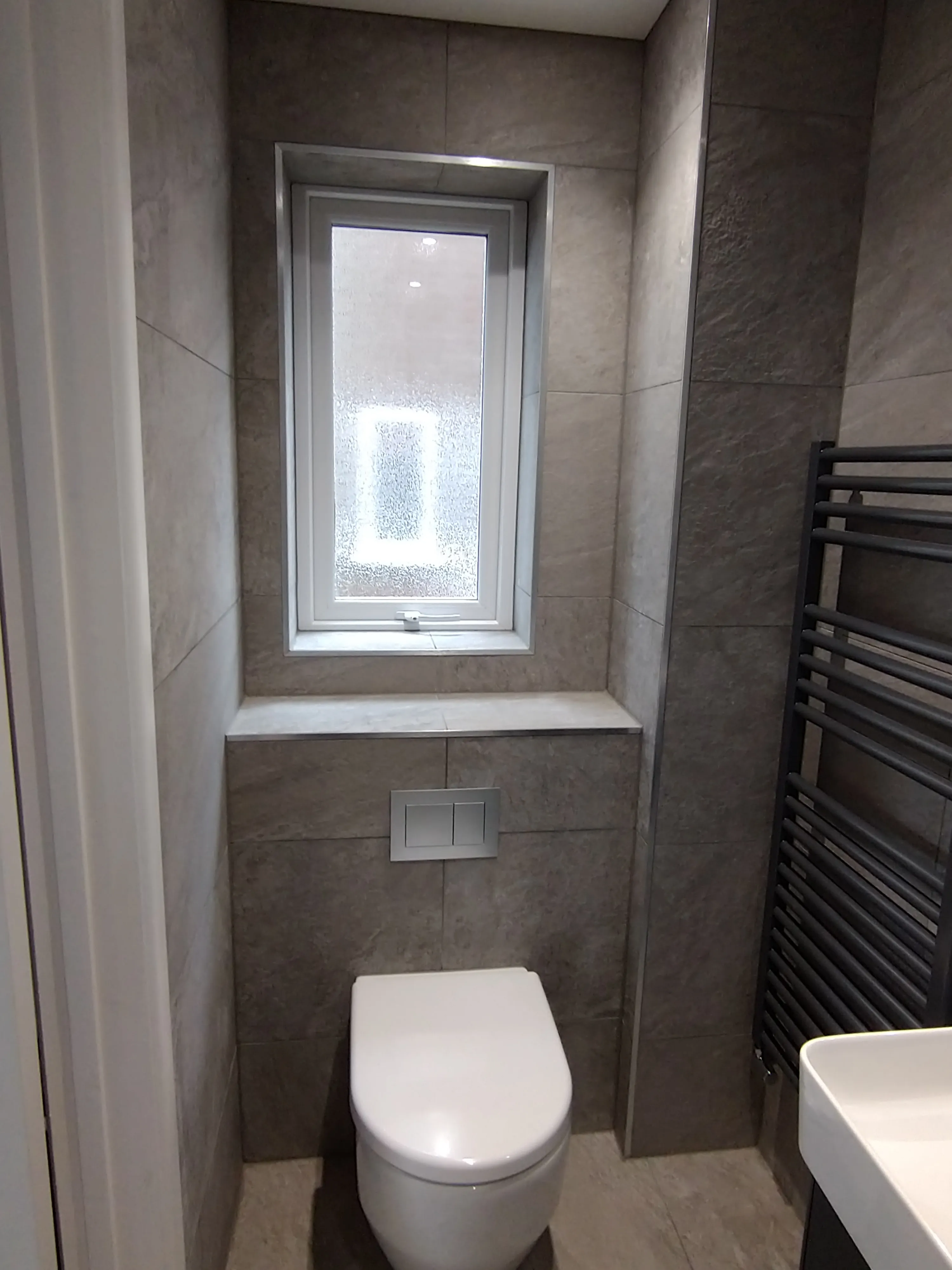 Luxury turnkey bathroom installation by Sands & Vossen featuring grey tiling and wall-hung toilet.