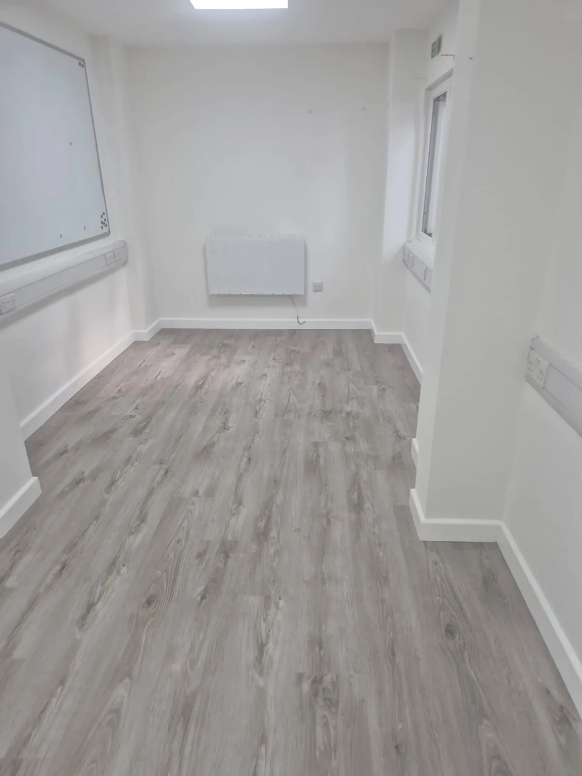 Interior view of a modern, empty commercial office after refurbishment, showing light grey flooring, white walls, and electrical trunking.