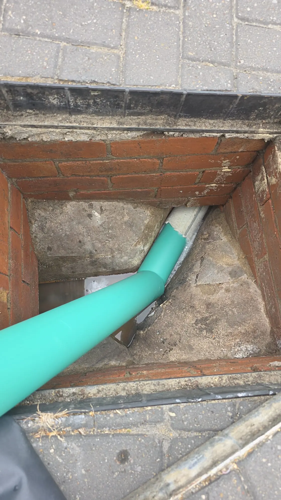 An inspection chamber showing a modern green plastic pipe being used for drain relining within an older, possibly ceramic, drain structure.