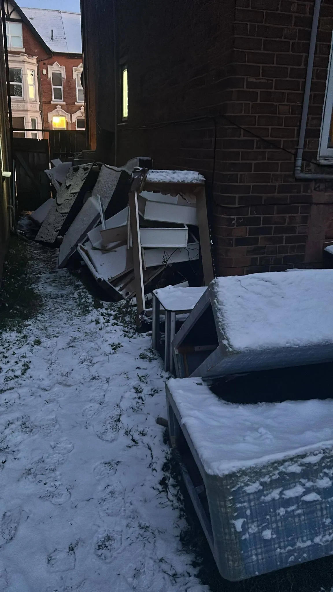 Bulky household rubbish and old furniture piled in a snowy side alley awaiting collection