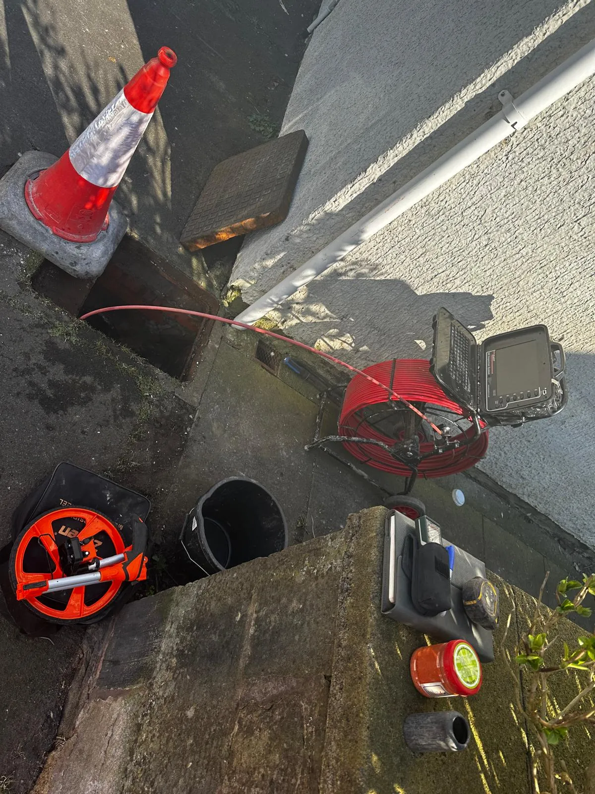 Drainage inspection in progress with CCTV camera equipment and a red traffic cone next to an open manhole.