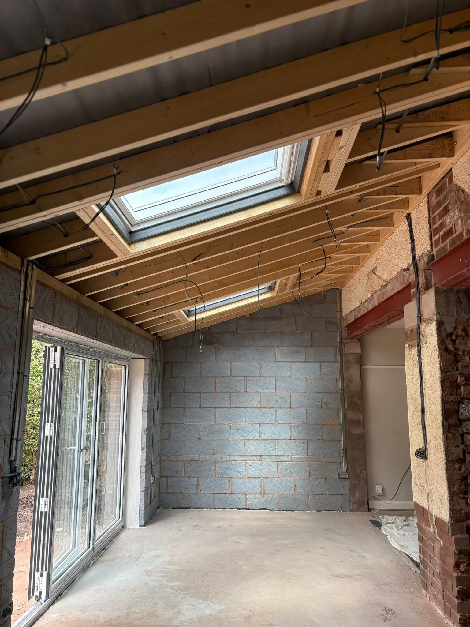 A home extension in the process of being built, with a new roof frame, skylights, bi-fold doors, and blockwork walls.