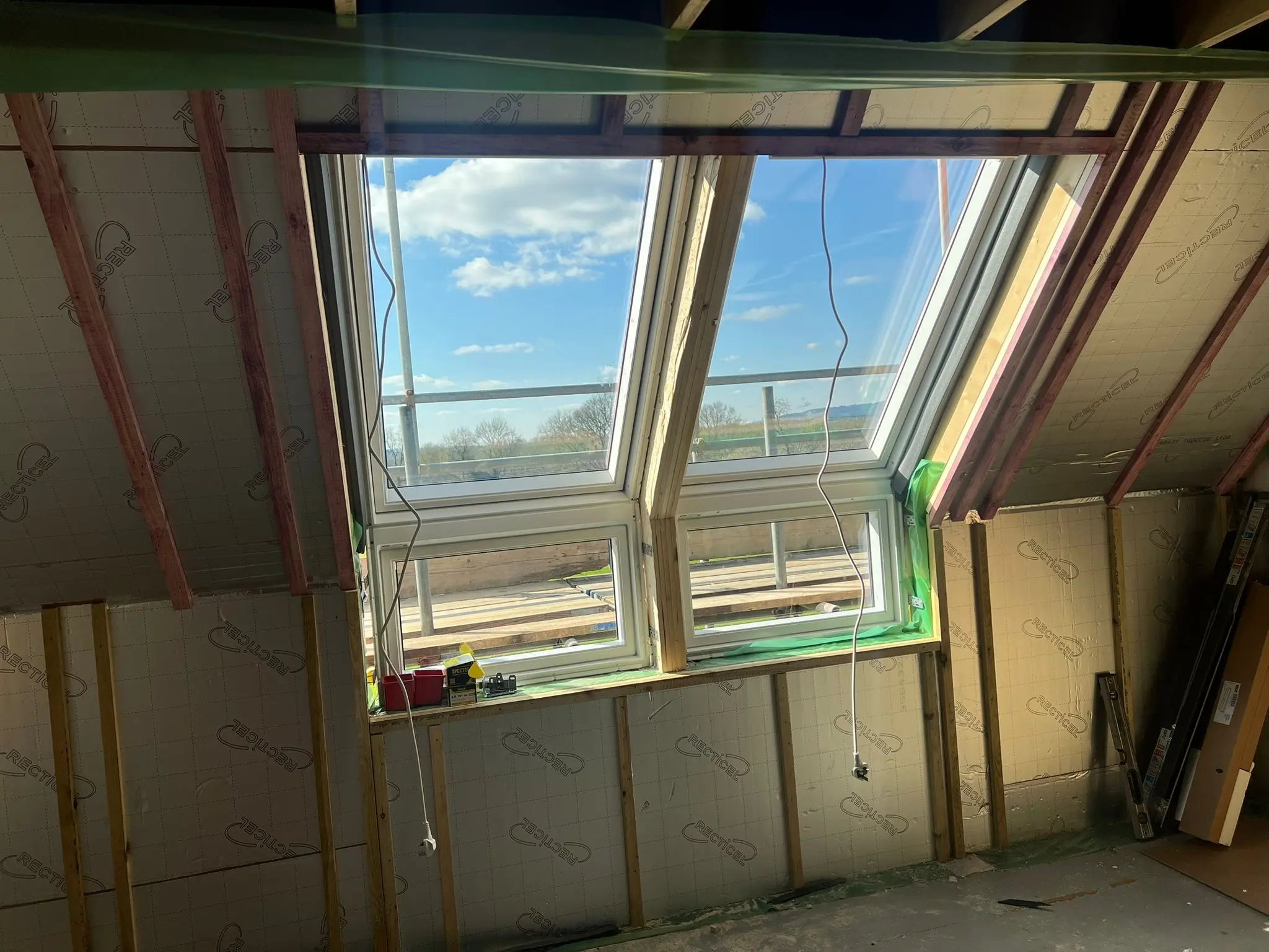 A newly installed double roof window in a building under construction with exposed timber framing and Recticel insulation