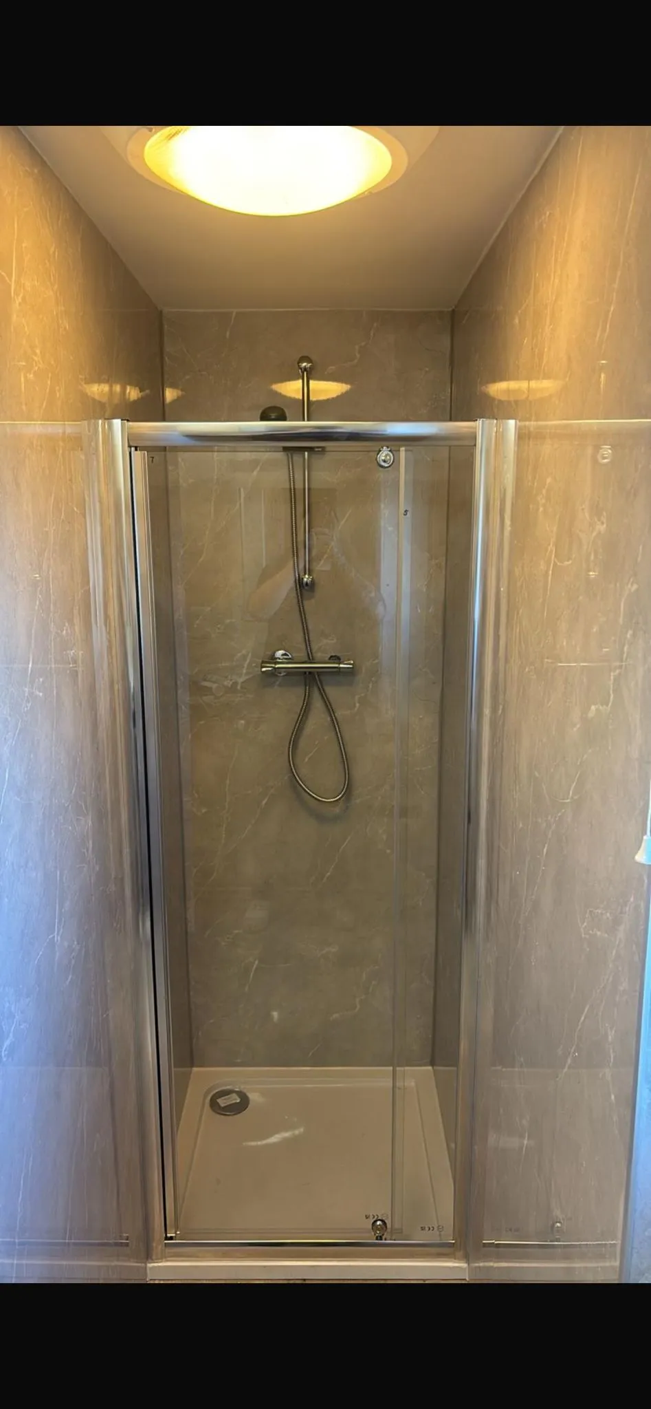 A clean, contemporary shower enclosure with marbled grey tiles, a glass door, and a shower head, highlighting bathroom installation services.