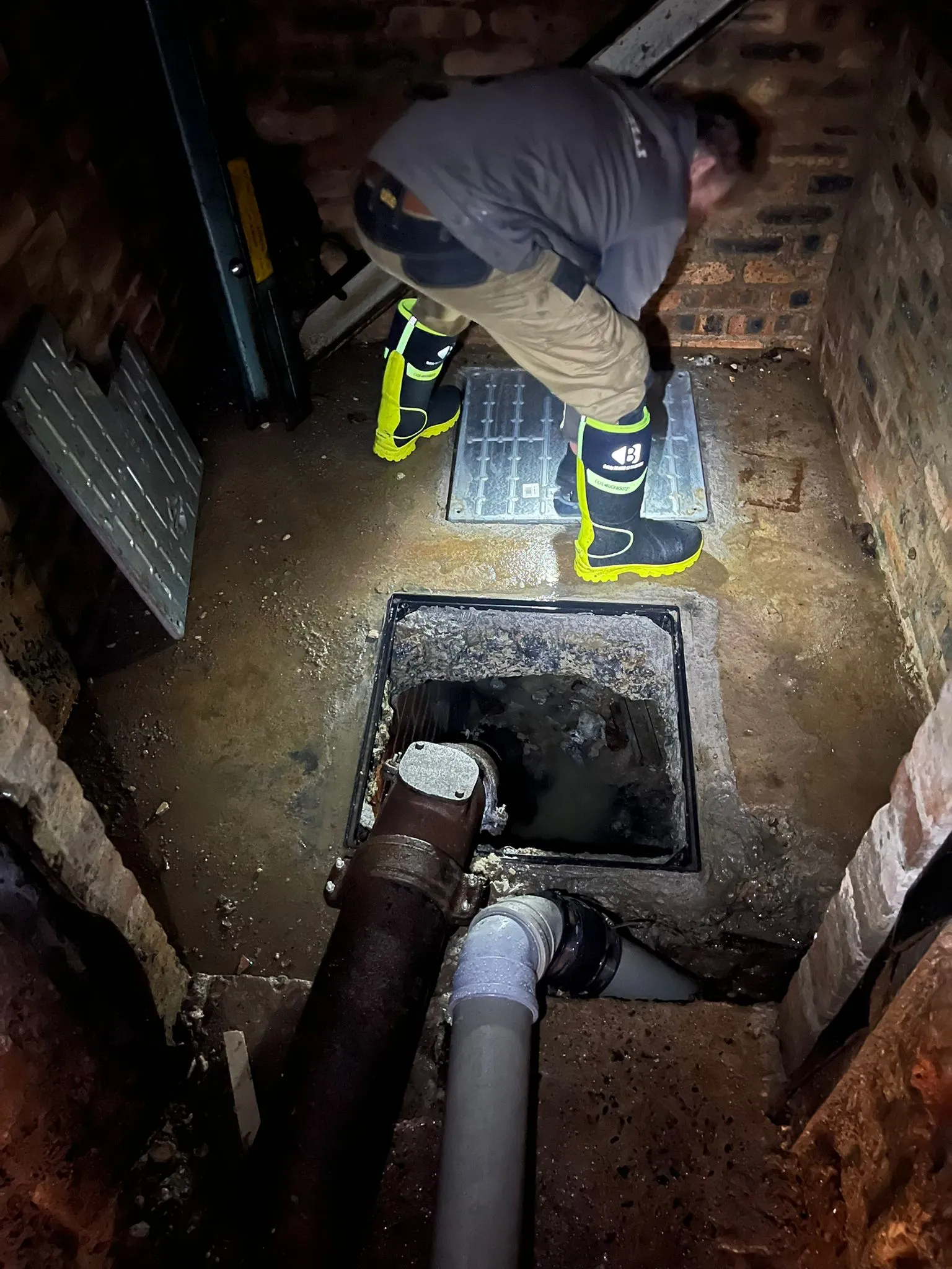 A drainage engineer from Go Flow Solutions Edinburgh in high-visibility boots inspecting an open drain or manhole.