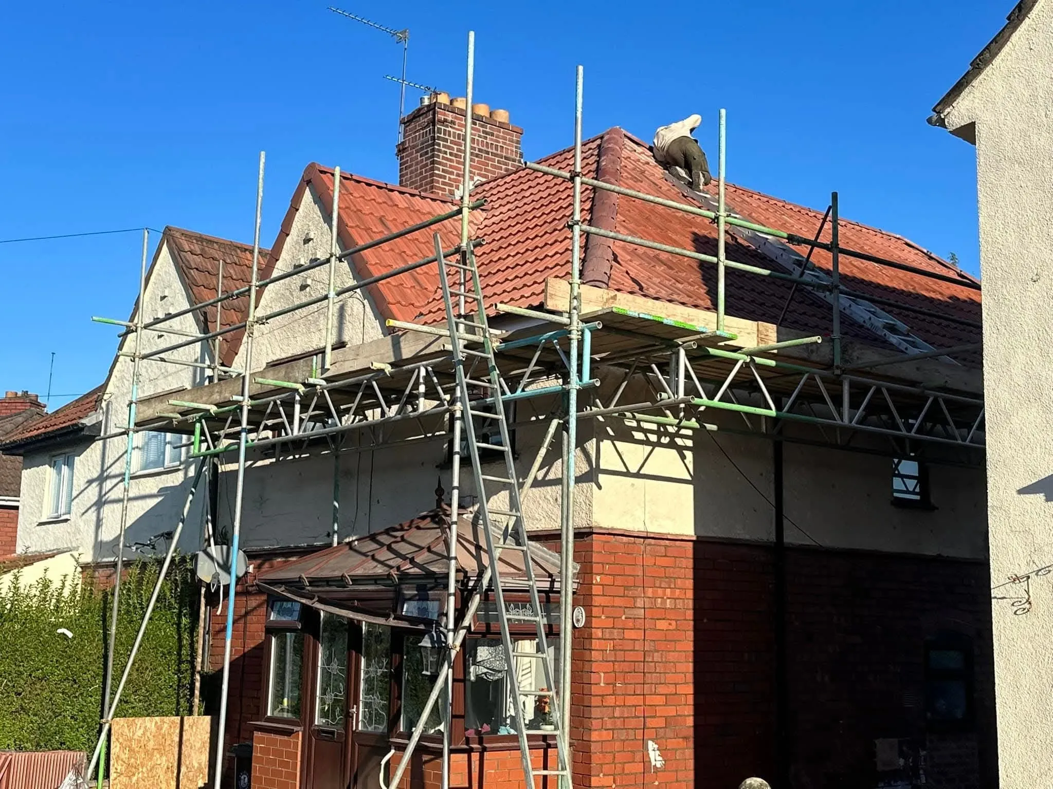 A roofer performing repairs on a red tiled house roof with scaffolding installed, representing domestic roofing services by NTL Roofing.