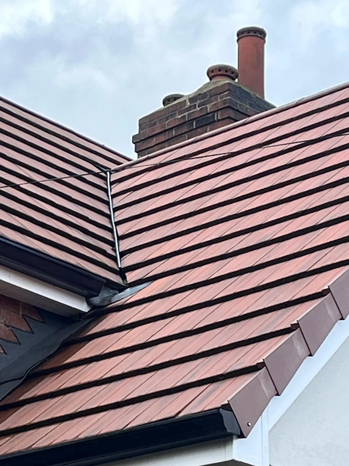 A close-up of high-quality red clay or concrete roof tiles on a residential pitched roof with a brick chimney stack