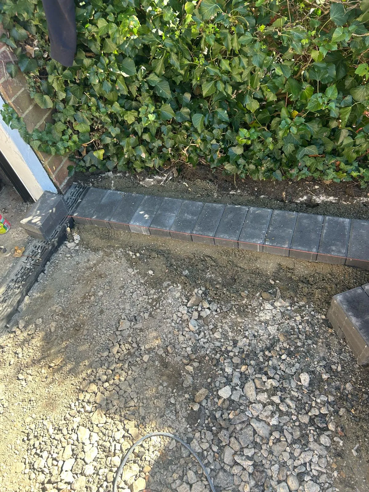 Work in progress: Block paving edging being laid on a prepared sub-base for a driveway or path, with an ivy hedge in the background.
