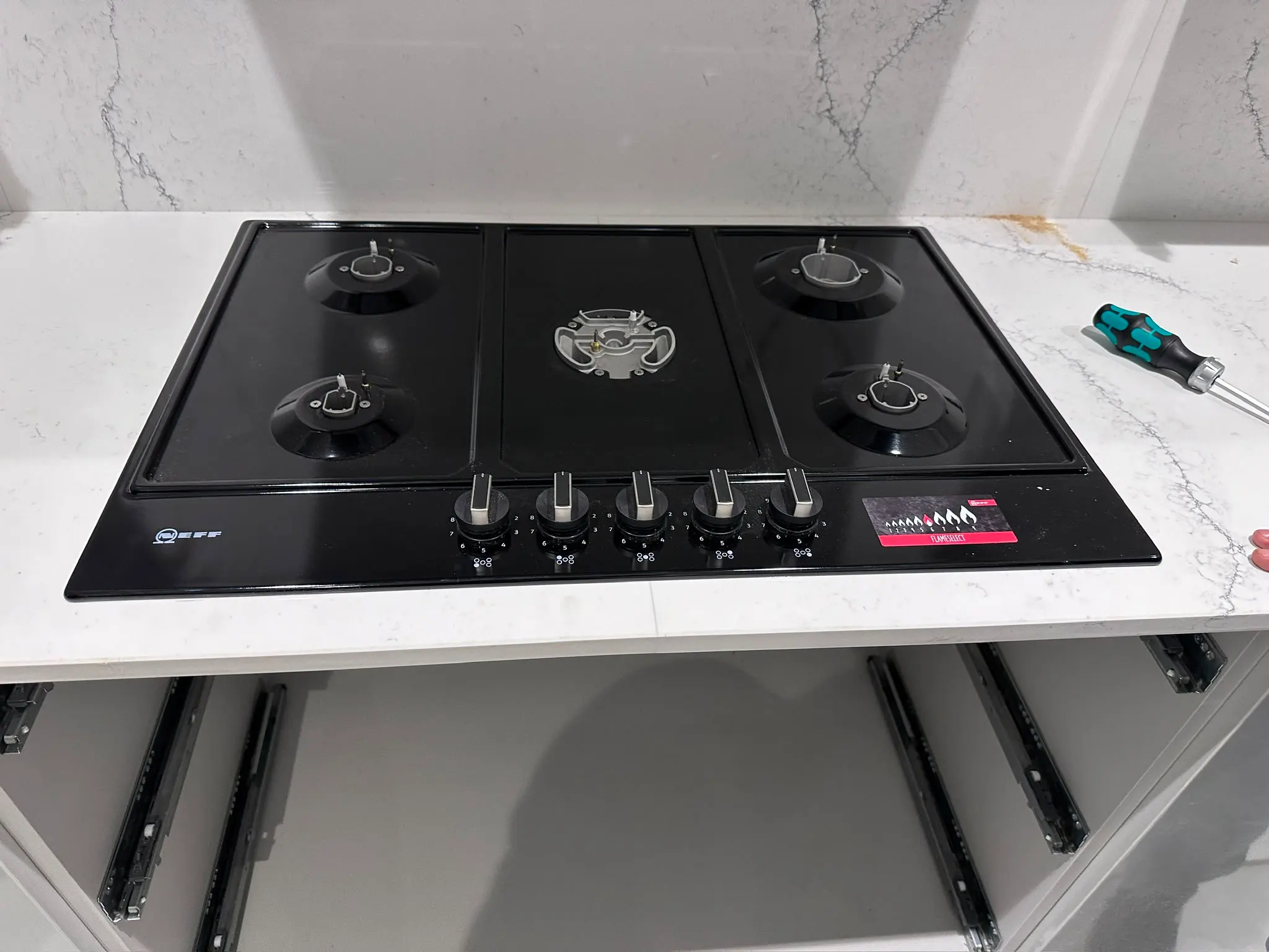 A newly installed black glass gas hob sitting on a white marble countertop.