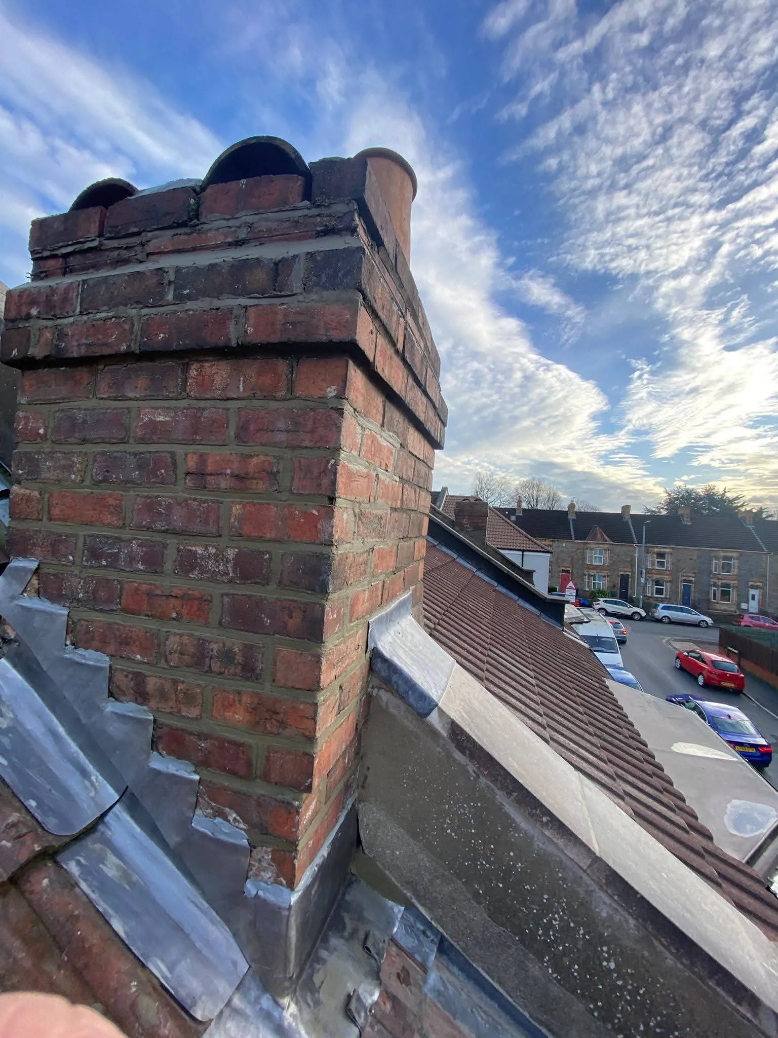 A brick chimney with lead flashing on a tiled roof in a residential area