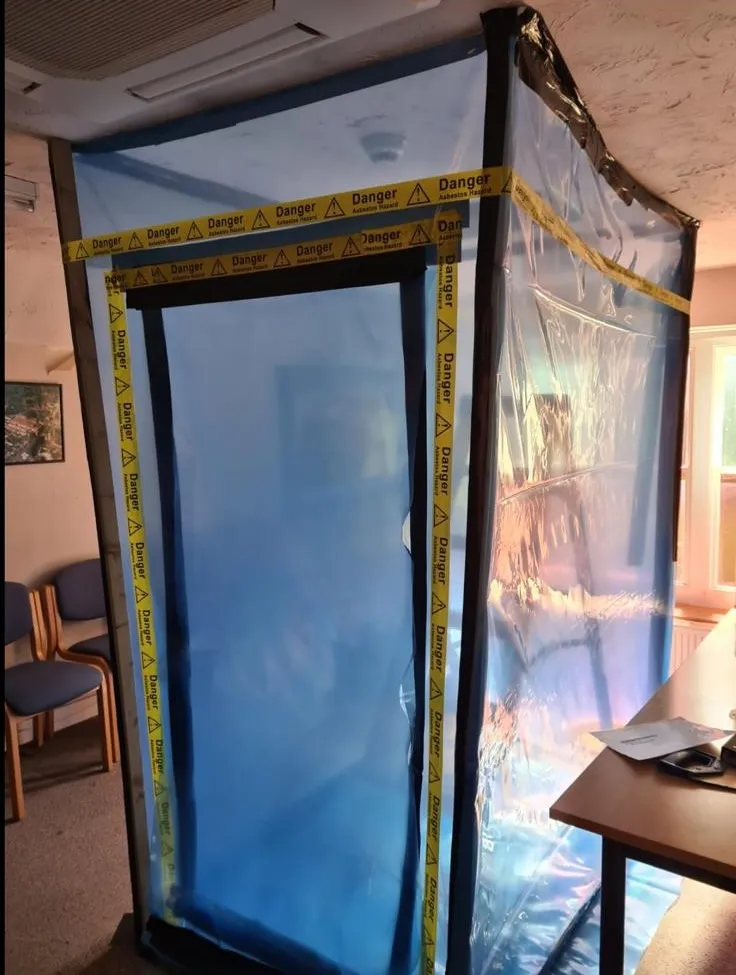 A blue plastic asbestos containment enclosure with yellow danger warning tape inside a property.