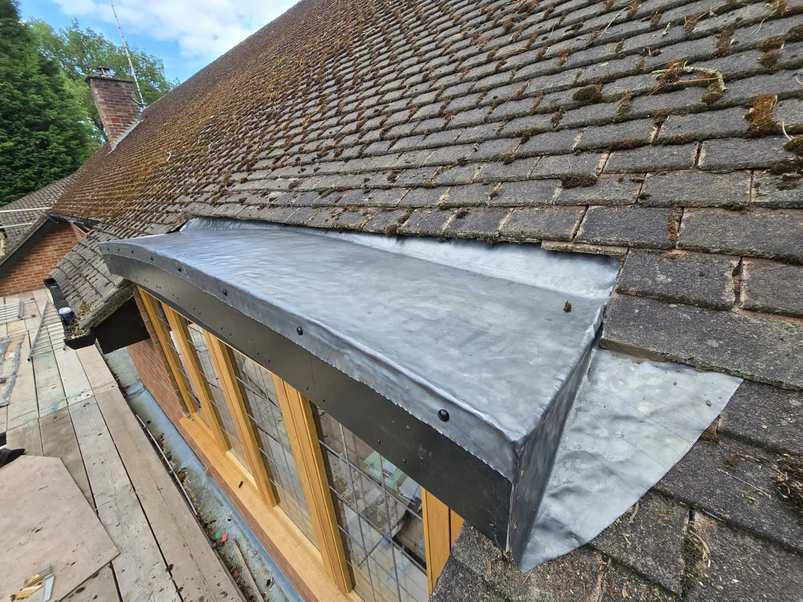 Close-up of new lead work and flat roof section on a dormer window, against an older, mossy tiled roof.
